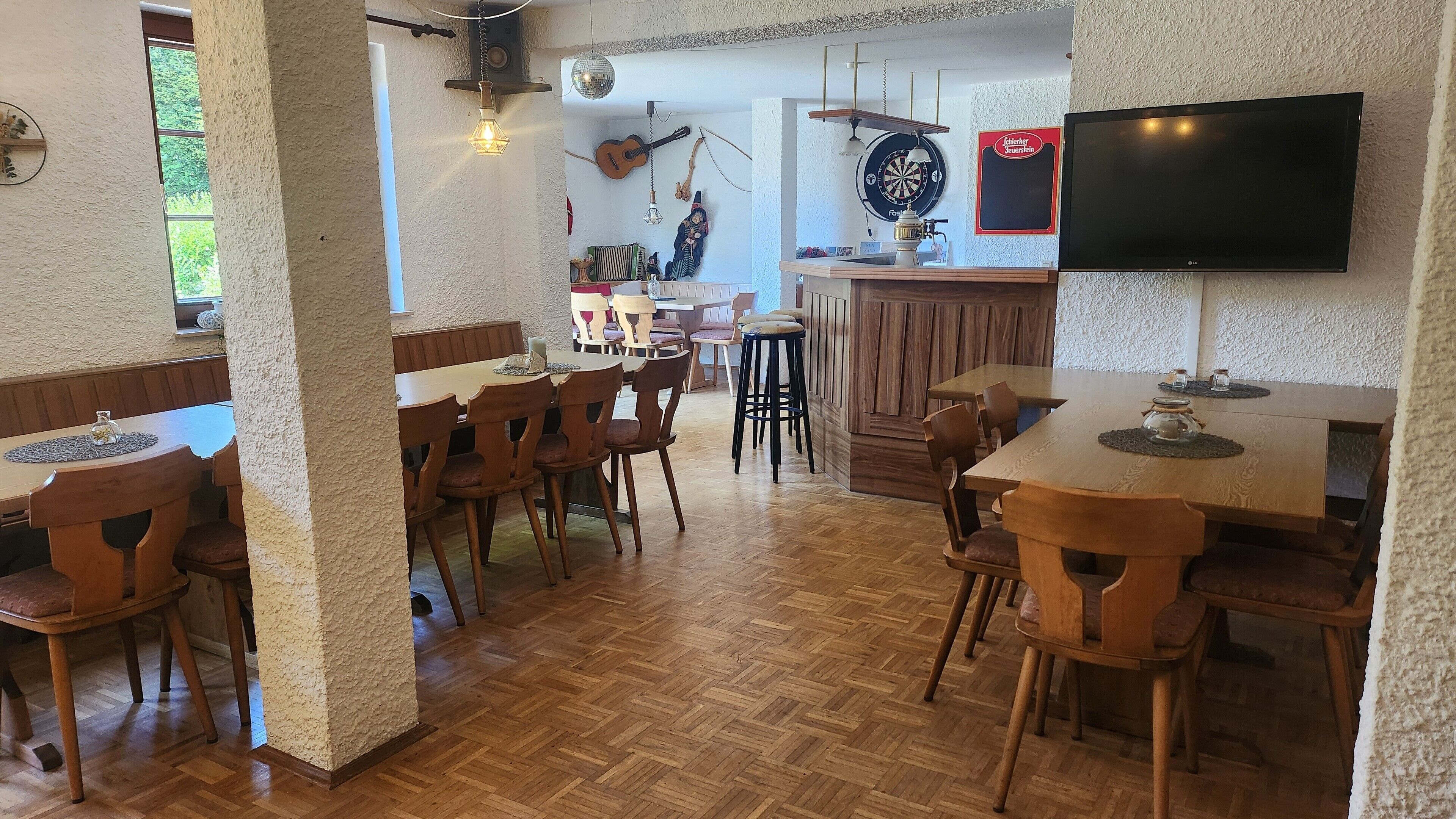 Ein Restaurant mit Holztischen und -stühlen, einer Dartscheibe, einer Gitarre und einem Fernseher.