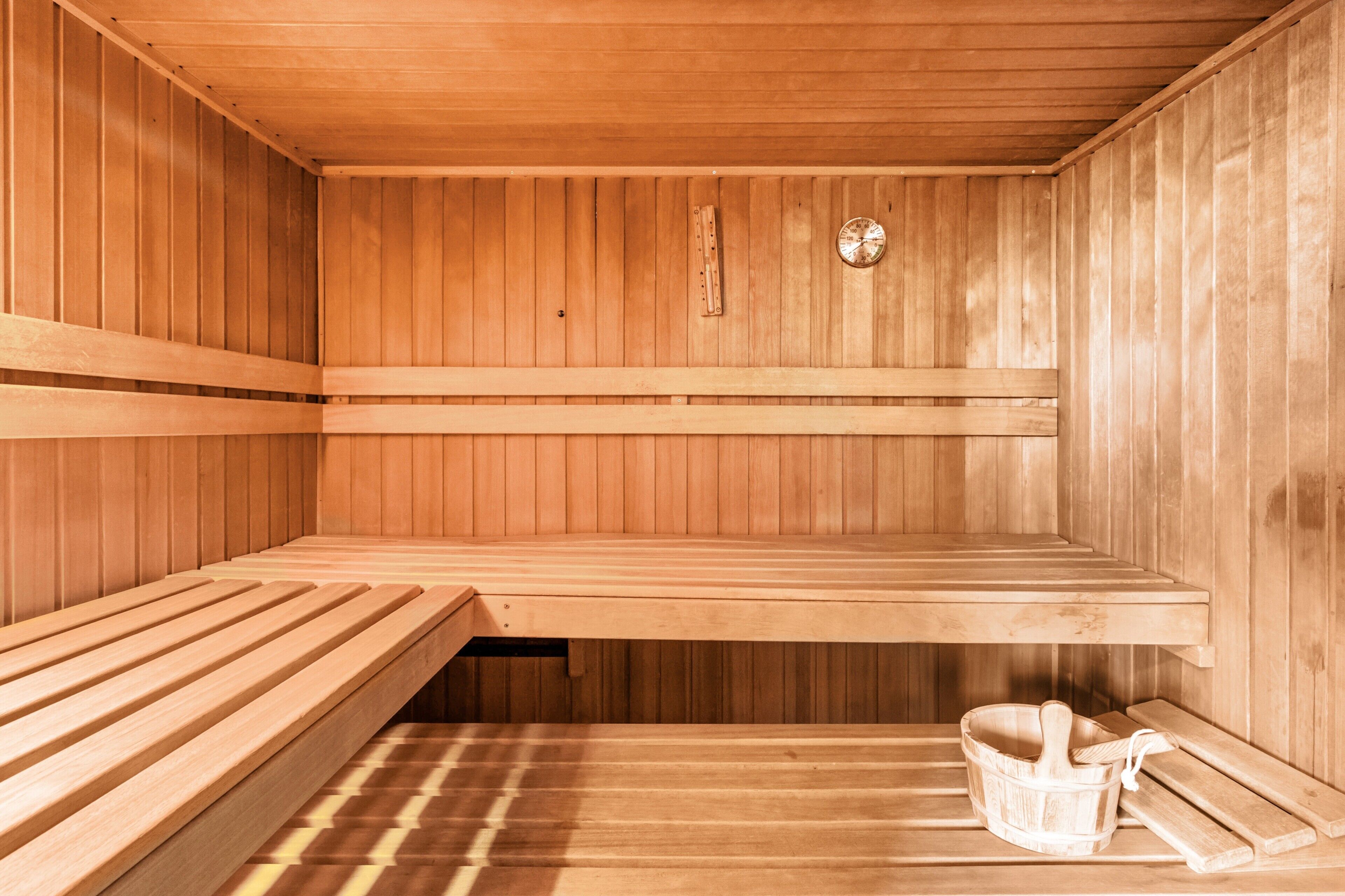 Eine Sauna mit Holzbänken, einem Holzeimer und einem an der Wand befestigten Thermometer.