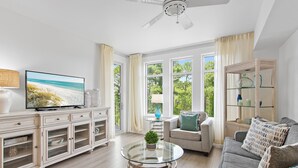 Uma sala de estar moderna com televisão, mesa de centro de vidro, sofá e estante.