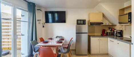 A modern kitchen with a dining area, large windows, and a flat-screen TV.