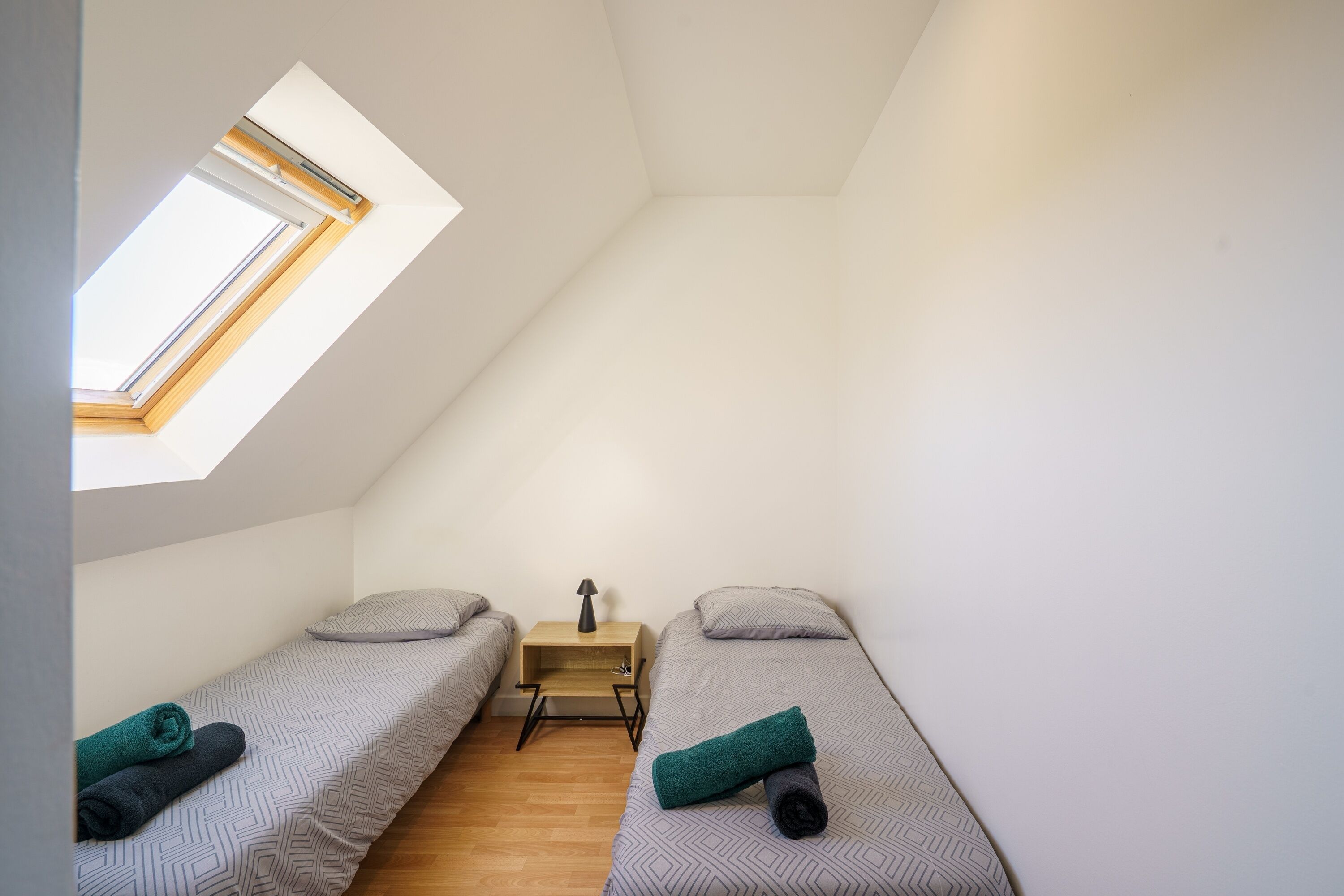 Een ruime, goed verlichte kamer met twee eenpersoonsbedden, een klein houten tafeltje en een dakraam.