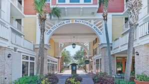 Der Eingang zum Village of Baytowne Wharf mit einem zentralen Bogen, Palmen und einem Pflasterweg.