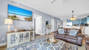Ein Wohnzimmer mit braunem Ledersofa, einem gemusterten Ottomanen und einem großen Gemälde, das eine Strandlandschaft zeigt.