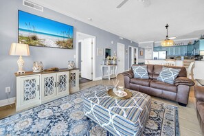 Ein Wohnzimmer mit braunem Ledersofa, einem gemusterten Ottomanen und einem großen Gemälde, das eine Strandlandschaft zeigt.