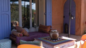 Un espacio al aire libre acogedor con cama, almohadas, una mesa con un libro y un jarrón decorativo.