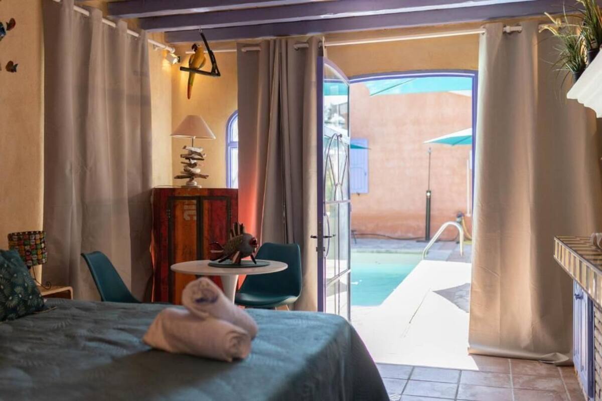 Une chambre d’hôtel avec un lit, une petite table avec une lampe, une chaise et une vue sur l’espace extérieur abritant une piscine.