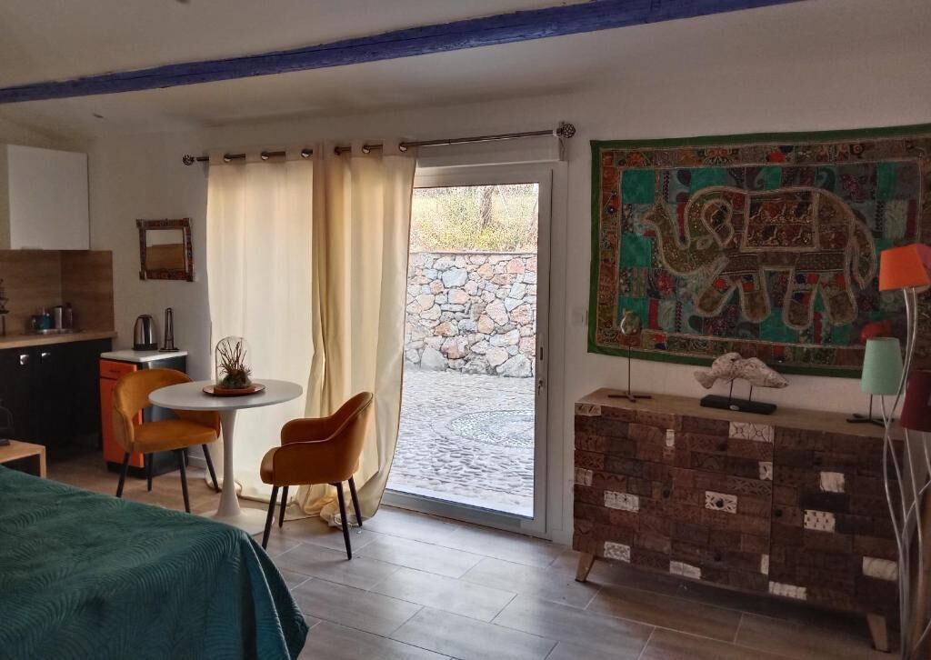 A room with a bed, a dining table with chairs, a kitchen area, a stone wall outside, and a decorative elephant painting.