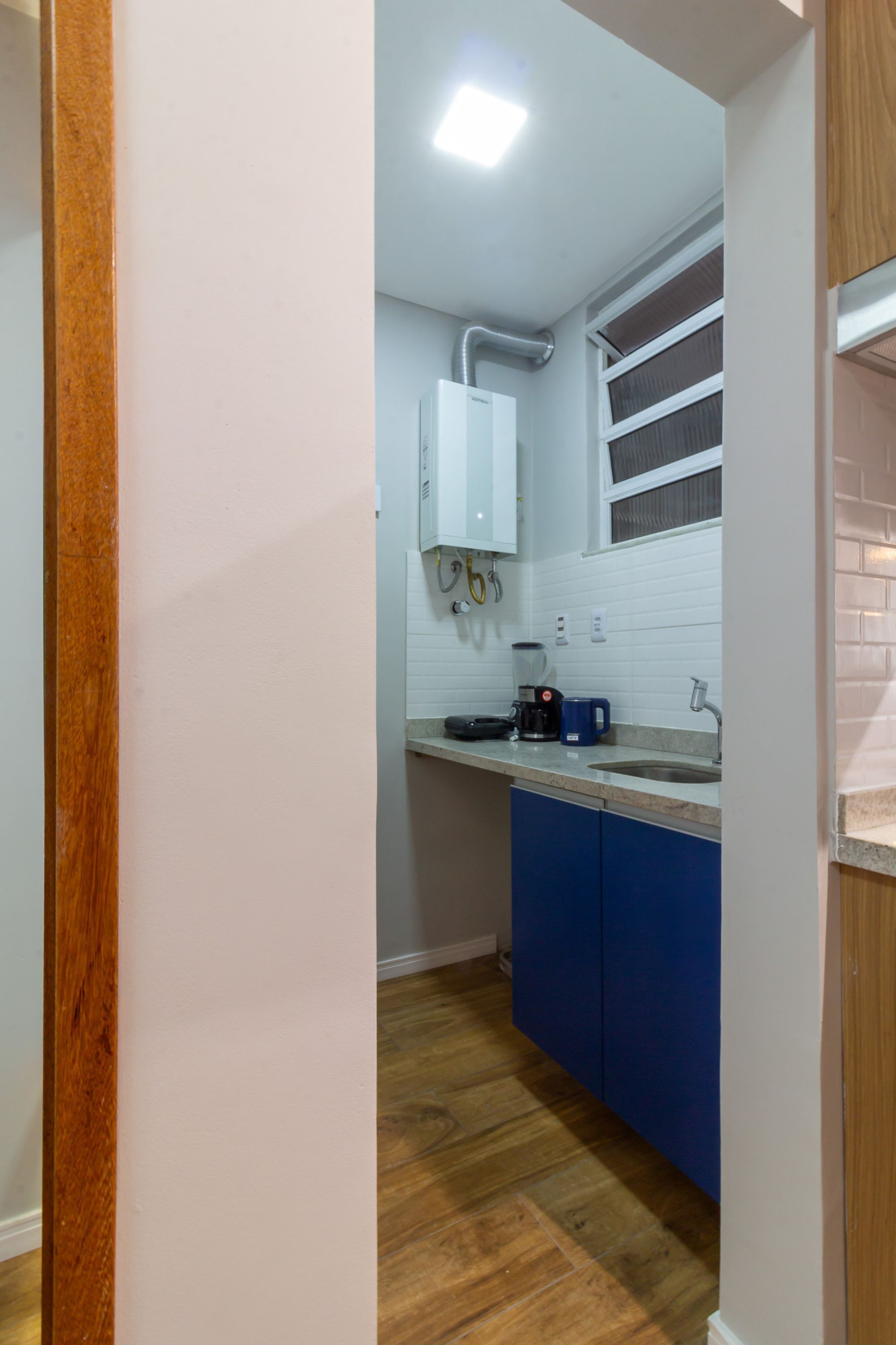 A narrow kitchen with white cabinets, a blue countertop, and a wooden floor.