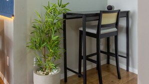 Et hjørneværelse med spisebord og stole, en potteplante, et billede i ramme på væggen og en lampe over bordet.