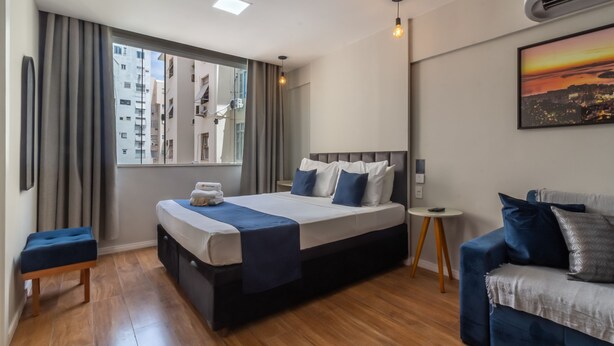 Et moderne hotelværelse med en stor seng, et lille natbord, en sofa og et vindue med gardiner.