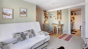 A living room with a sofa, a dining table with chairs, a kitchen area, and a hallway leading to another room. - Studio 'Prey Sabeyran' with Mountain View, Shared Terrace and Garden (Puy-Saint-Vincent)