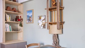 A wooden dining table with a metal plate, a wooden bookshelf with books and decorative items, and two framed pictures on the wall. - Studio 'Prey Sabeyran' with Mountain View, Shared Terrace and Garden (Puy-Saint-Vincent)