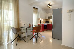 A modern kitchen with a dining area, featuring a glass table, two chairs, a refrigerator, and a microwave. - Athenian Riviera Prestige 2 bedroom (Glifada)