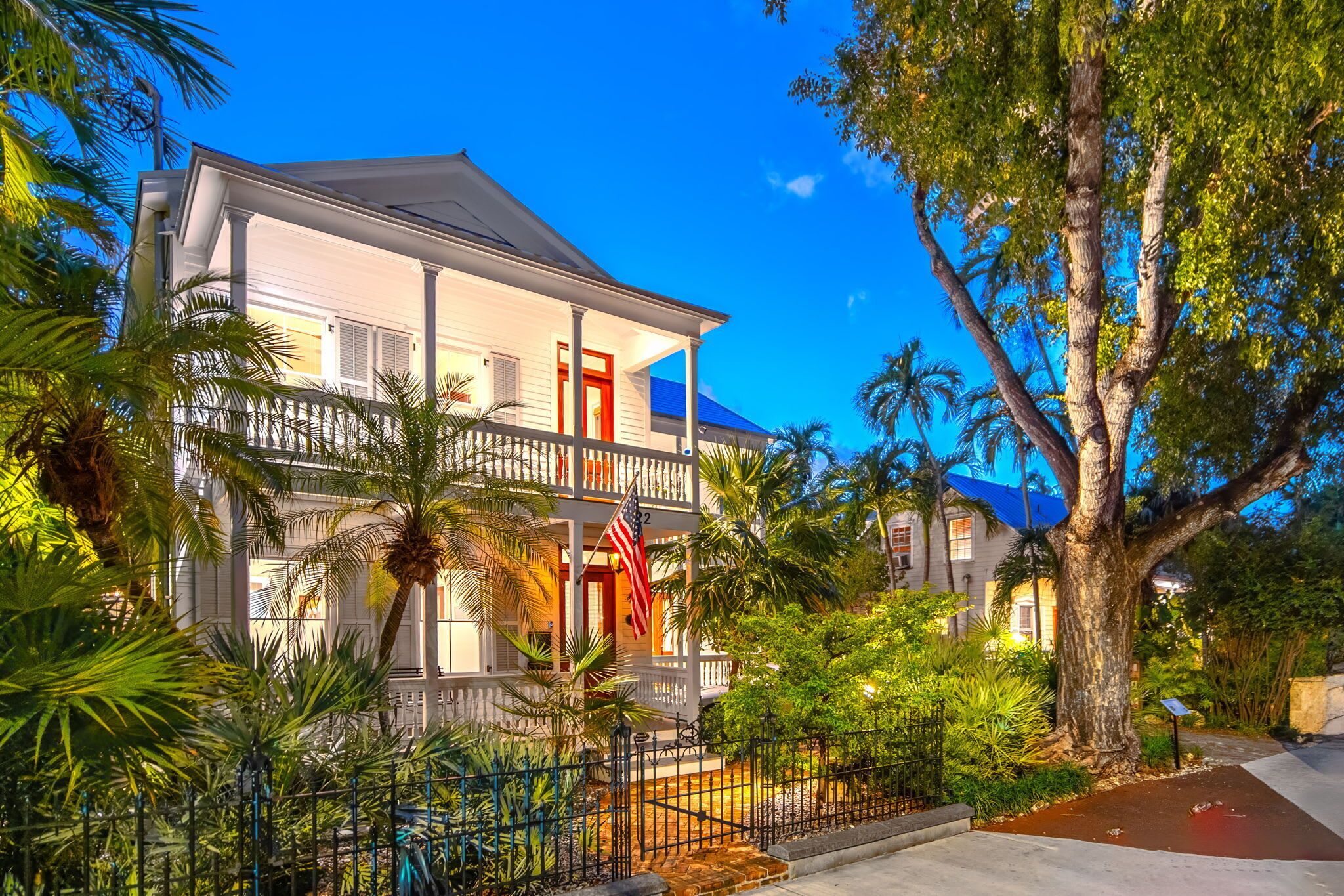 A two-story colonial-style building with a balcony, surrounded by lush tropical vegetation and a clear blue sky.