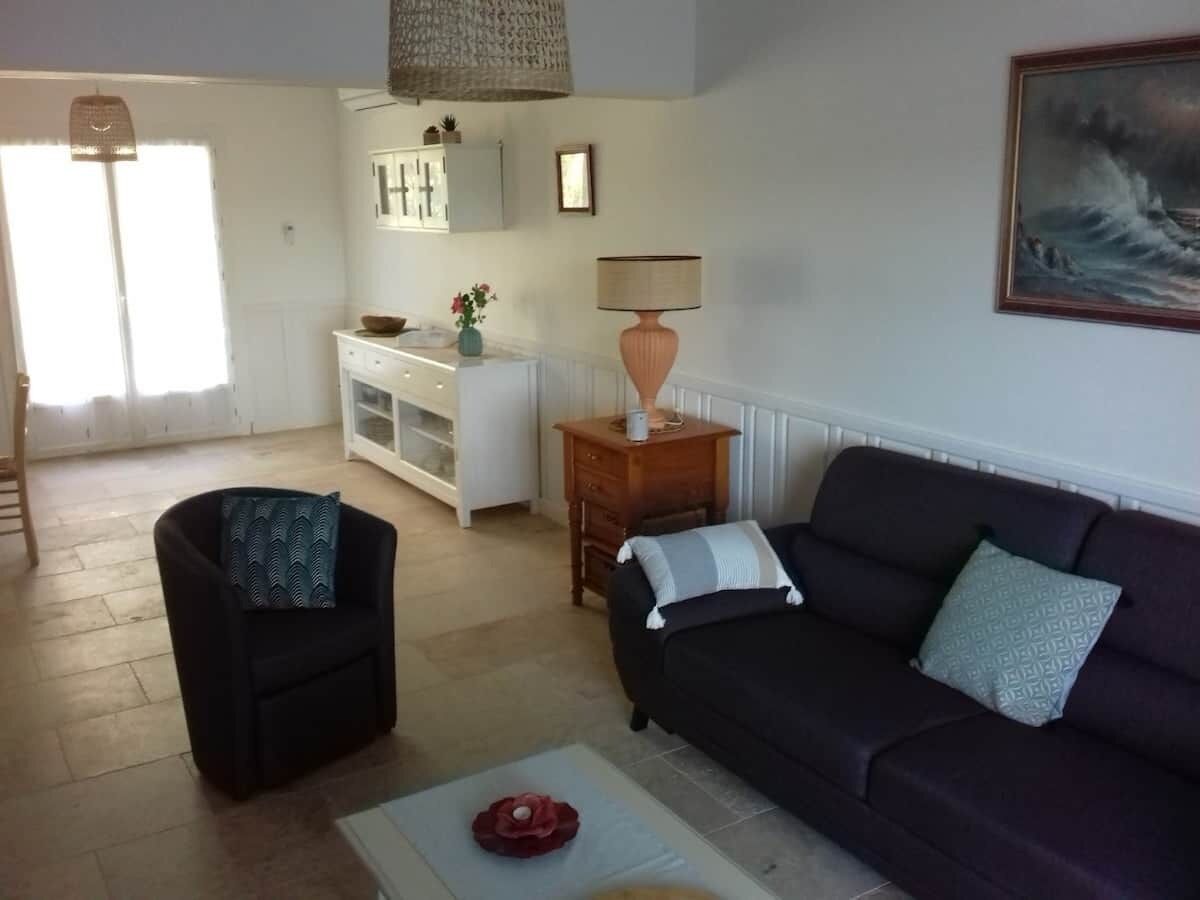A living room with a dark sofa, a black armchair, a wooden side table with a lamp, and a white cabinet.