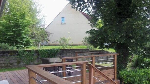 Una terraza de madera con barandillas de metal, un sendero de piedra y una casa al fondo.