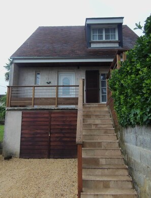 A two-story house with a wooden staircase leading to a front door, a garage, and a small balcony with a railing. - Maison avec jardin à 2 minutes à pied du centre (Sarlat-la-Canéda)