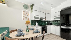 A modern kitchen with white cabinets, a black refrigerator, and a dining area with a round table and chairs. - Comfortable Apartment | Garden and Private Parking (Szczecin)
