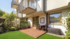 A modern apartment with a wooden deck, a dining area, and a large window. - Comfortable Apartment | Garden and Private Parking (Szczecin)