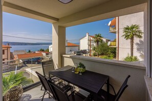 Ein Balkon mit Tisch, Stühlen und Blick auf das Meer und umliegende Geb äude.