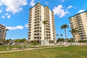 A high-rise hotel with multiple balconies, a well-maintained lawn, and palm trees. - 🌊Beachfront Beauty | Amazing Amenities | Estero Beach and Tennis 1102-A🌊 (Fort Myers Beach)