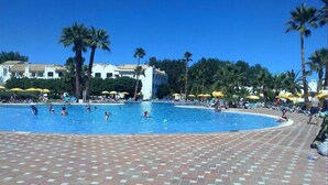 Una piscina con pavimento piastrellato, palme e ombrelloni.