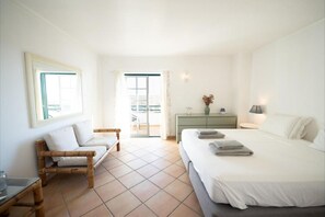 Habitación de hotel con cama, sofá, cómoda y balcón.