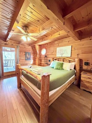 Un dormitorio de cabaña de madera con cama, mesita de noche, cómoda y ventilador de techo.