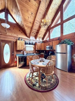 Interior de una cabaña de madera con una mesa de comedor, sillas, un refrigerador y una zona de cocina.