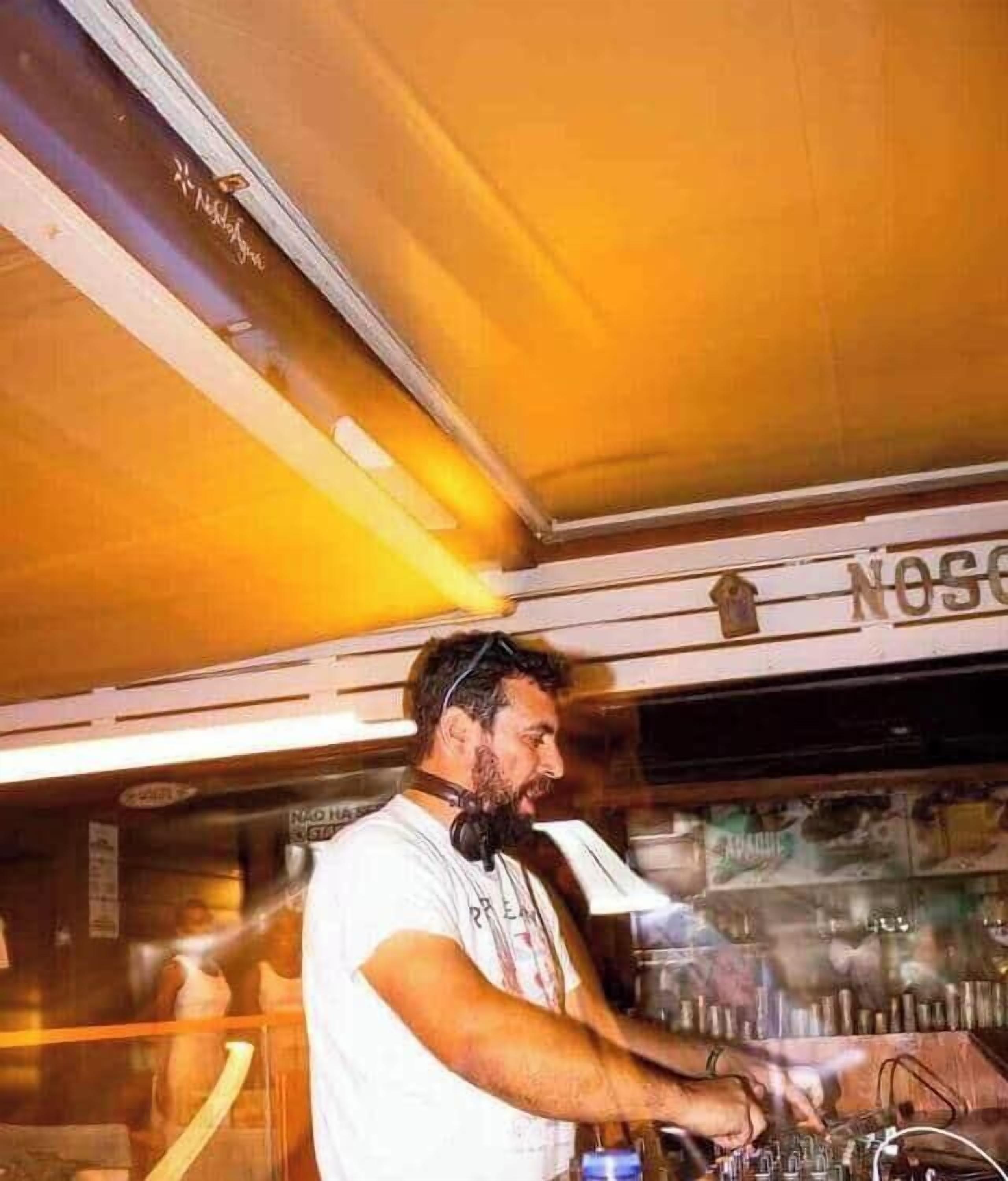 Iemand bedient DJ-apparatuur in een ruimte met een bord waarop 'NOSC' staat.