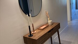 A hallway with a wooden console table, a round mirror, and a wall-mounted light fixture. - Delgado Alves Apartment (Quarteira)