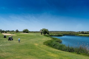 Um campo de golfe com um corpo de água, uma ponte e um céu limpo.