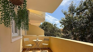 A balcony with a tiled floor, a hanging plant, a table with chairs, and a window. - Delgado Alves Apartment (Quarteira)