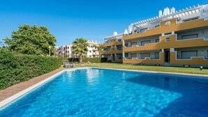 A swimming pool with clear blue water, surrounded by greenery and modern buildings with balconies. - Delgado Alves Apartment (Quarteira)