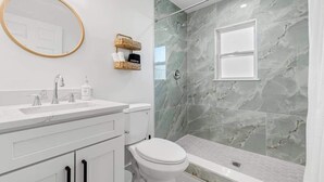 A modern bathroom with a marble shower wall, a white sink, and a toilet.
