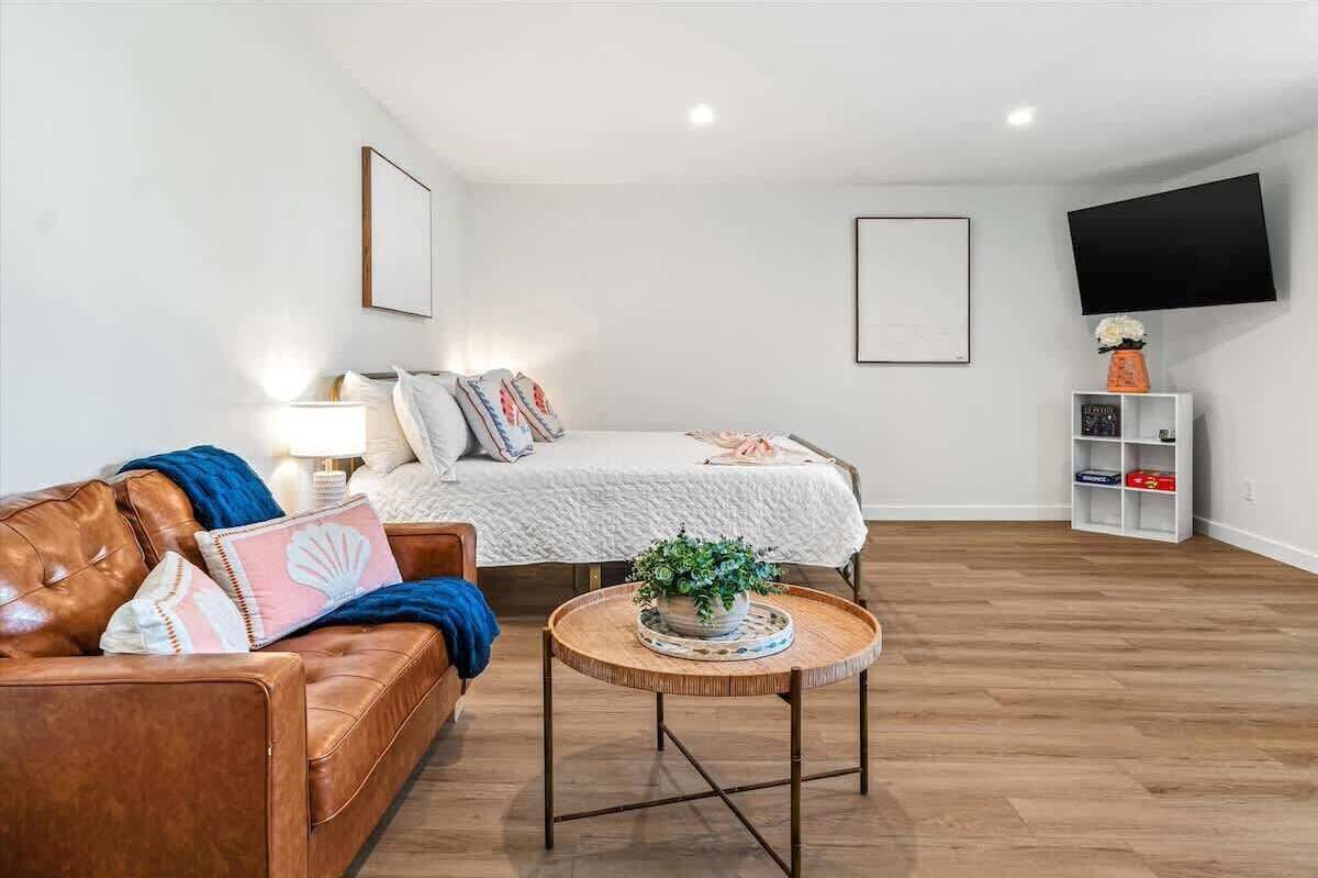 A modern bedroom with a bed, a leather sofa, a bedside table with a plant, and a TV mounted on the wall.