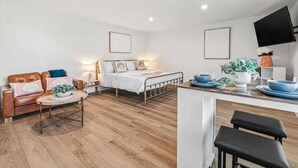 A modern, compact living space with a bed, a sofa, a dining area, and a kitchen.