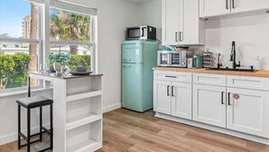 A modern kitchen with white cabinets, a teal refrigerator, a microwave, and a wooden countertop.