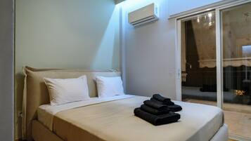 A hotel room with a bed, white pillows, a folded towel, an air conditioning unit, and a sliding glass door leading to an outdoor area.