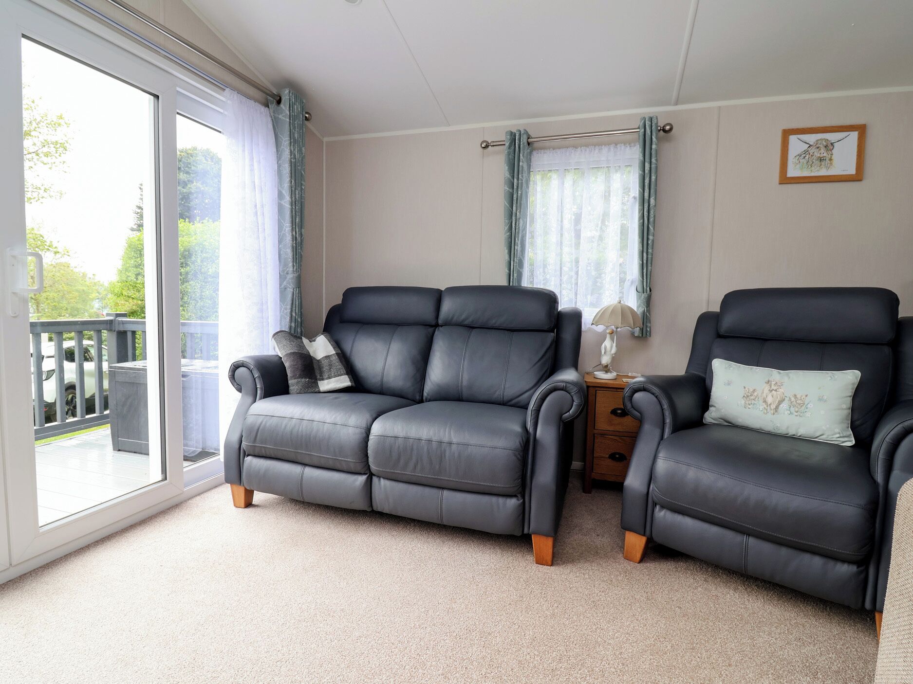 A room with two black leather sofas, a small wooden nightstand, and a large sliding glass door leading to a balcony.