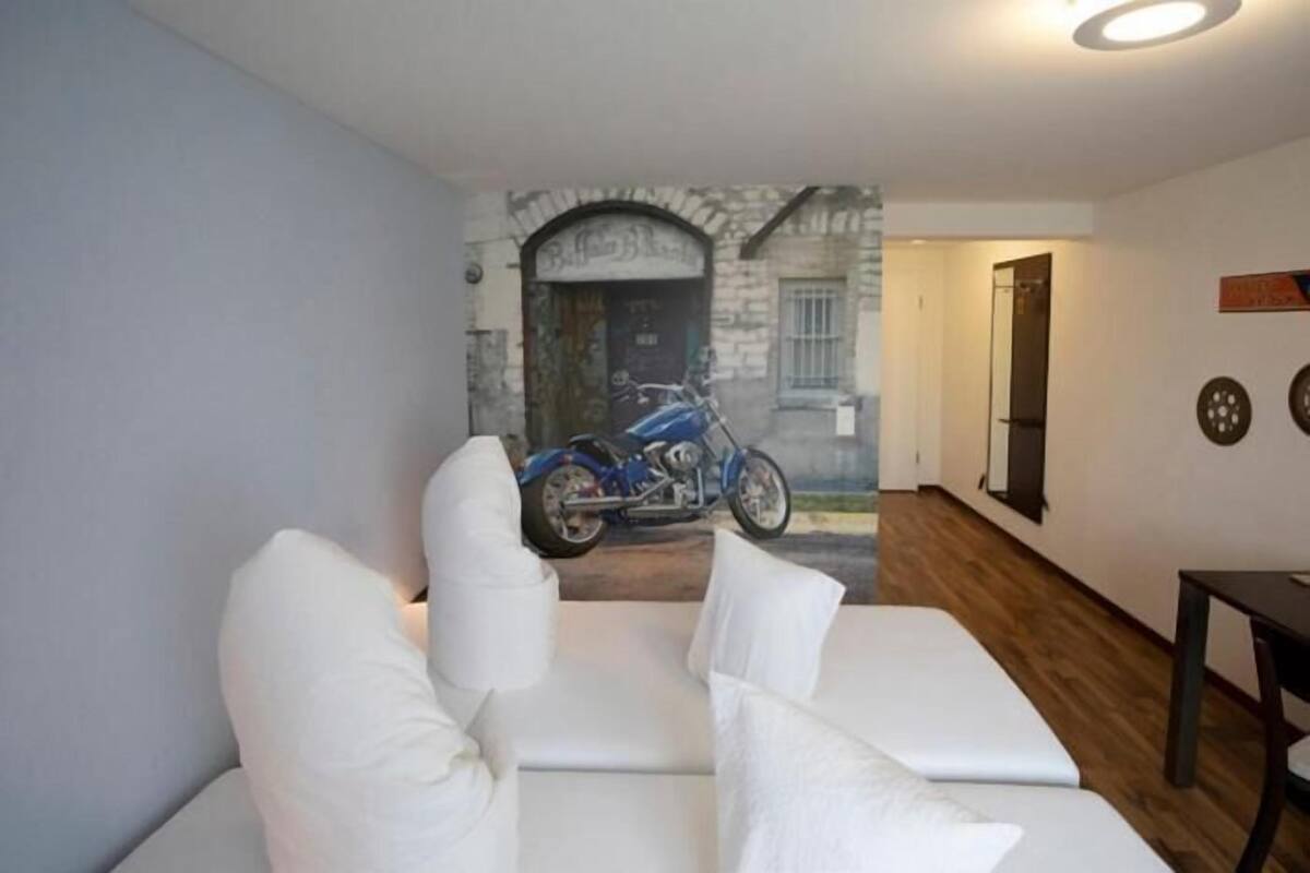 A room with a white sofa, a motorcycle in the background, and a wooden floor.