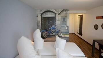 Una stanza con un divano bianco, una motocicletta sullo sfondo e un pavimento in legno.