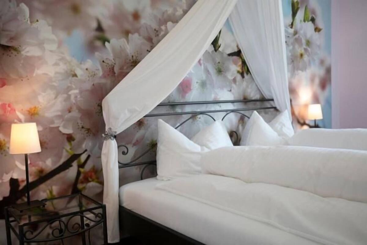 A bed with white bedding, a canopy, and a floral wallpaper background.