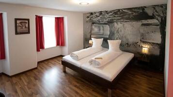 A bedroom with a bed, a window with red curtains, a stone wall, and a wooden floor.