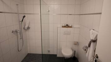 Um banheiro pequeno e moderno, com box de vidro, vaso sanitário e porta-toalhas.