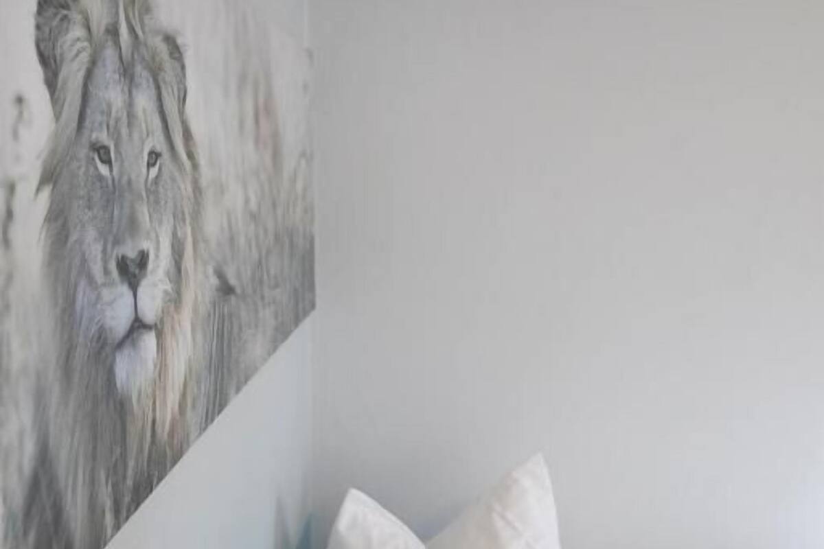 A bedroom with a bed, pillows, and a wall painting of a lion.