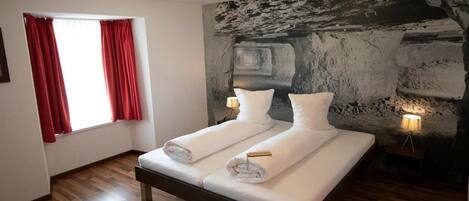 A room with a bed, two bedside lamps, a window with red curtains, and a textured wall.