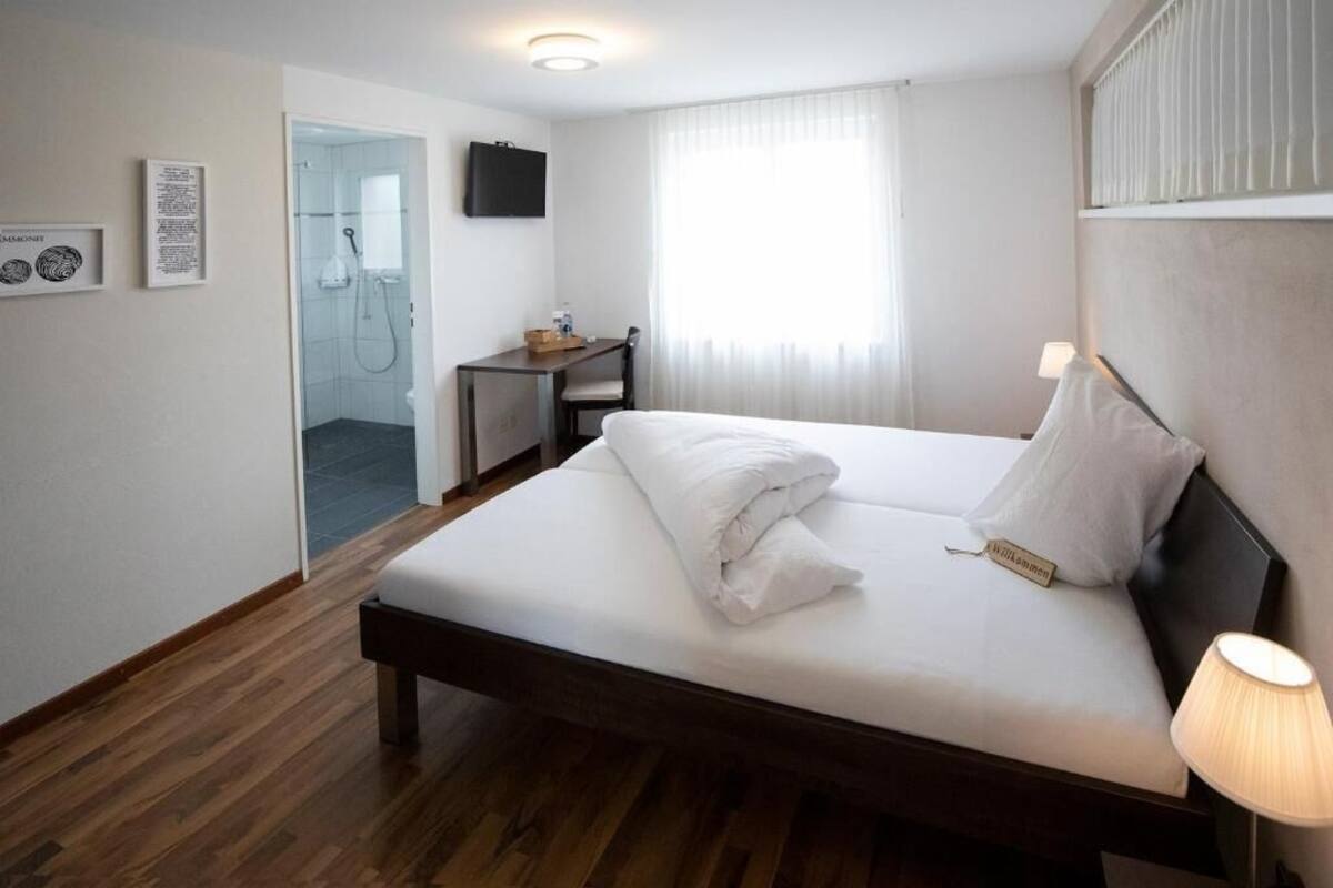 A hotel room with a bed, a desk, a TV, and a shower area.