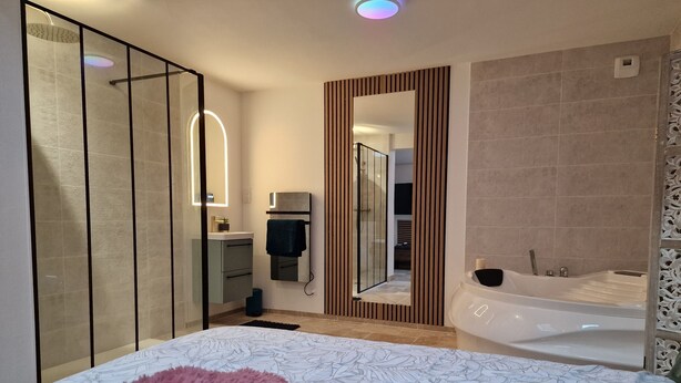 Ein modernes Schlafzimmer mit einem großen Bett, einem eigenen Badezimmer mit Badewanne und einem begehbaren Kleiderschrank.