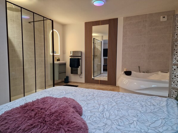 A modern bedroom with a large bed, a separate bathroom with a bathtub, and a walk-in closet.
